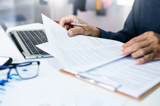 Foto: Person mit Dokumenten und Laptop